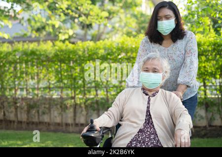 Aidez la vieille femme asiatique âgée ou âgée sur un fauteuil roulant électrique et portant un masque facial pour protéger l'infection de sécurité Covid-19 coronavirus dans le parc. Banque D'Images