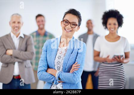 J'ai trouvé le bon endroit pour moi. Belle jeune femme souriant à l'appareil photo avec des collègues en arrière-plan. Banque D'Images