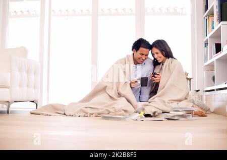 Pour tirer le meilleur parti de leur temps ensemble. Photo d'un jeune couple assis sur le sol enveloppé dans une couverture regardant des albums photo. Banque D'Images