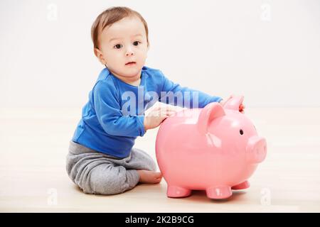 Je suis déjà en train de planifier mon avenir. Studio portrait d'un bébé garçon jouant avec une porcgybank. Banque D'Images