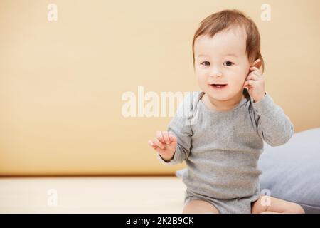 HES un petit gars heureux. Portrait d'un adorable bébé garçon assis sur le sol et souriant à l'appareil photo. Banque D'Images