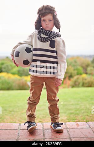 Pluie ou brillance. Photo d'un petit garçon debout à l'extérieur avec son ballon de football. Banque D'Images