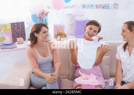 C'est parfait. Une jeune femme enceinte recevant des vêtements de bébé de ses jolies amies à sa douche de bébé. Banque D'Images