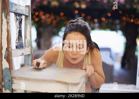 Le ponçage des antiquités est amusant. Une jeune femme sablant une chaise ancienne. Banque D'Images