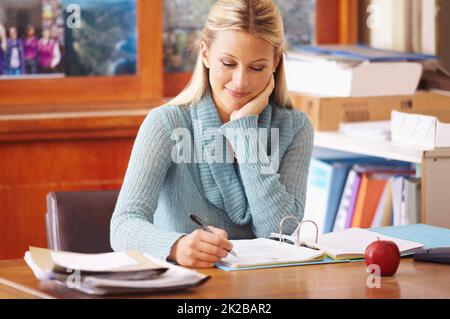 Marquage des devoirs. Une jeune enseignante marquant des documents d'examen dans son bureau. Banque D'Images