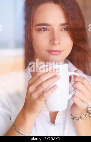 Café et contemplation. Une jeune femme qui a l'air réfléchie tout en buvant son café du matin. Banque D'Images