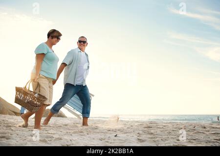 J'espère que vous avez emballé le champagne. Photo d'un couple à la plage avec un panier de pique-nique et des chaises. Banque D'Images