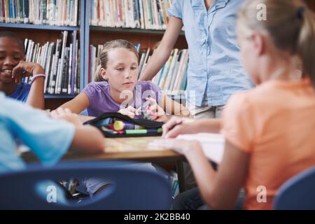 Se concentrer sur son travail. Une jeune fille assise à la bibliothèque avec ses camarades de classe et son professeur. Banque D'Images