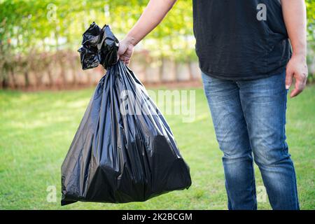 Femme tenant des sacs poubelle en plastique noir de déchets sur la chaussée, concept d'environnement propre. Banque D'Images