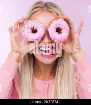 Shes aller des noix. Une femme tenant des beignets devant ses yeux tandis qu'isolée sur rose Banque D'Images