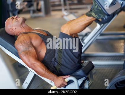 Se sentir déterminé. Plan d'un bodybuilder masculin faisant des exercices de jambe sur une machine à la salle de gym. Banque D'Images