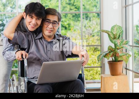 père homme assis en fauteuil roulant et son fils parlant des appels vidéo conférence sur ordinateur portable Banque D'Images