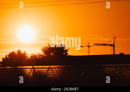 La silhouette haute de grue de construction dans le ciel orange coucher de soleil montre le chantier de construction avec l'ingénierie pour les bâtiments modernes et le développement de la ville comme travail d'équipe architectural pour les lignes de haute tension de gratte-ciel Banque D'Images