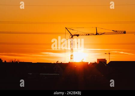 La silhouette haute de grue de construction dans le ciel orange coucher de soleil montre le chantier de construction avec l'ingénierie pour les bâtiments modernes et le développement de la ville comme travail d'équipe architectural pour les lignes de haute tension de gratte-ciel Banque D'Images