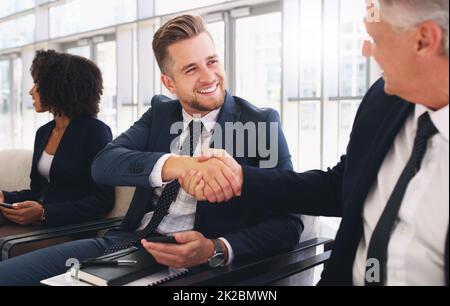 Bonjour, c'est un plaisir de vous rencontrer. Photo courte d'un beau jeune homme d'affaires qui se secoue la main avec un collègue tout en étant assis dans une file d'attente au bureau. Banque D'Images