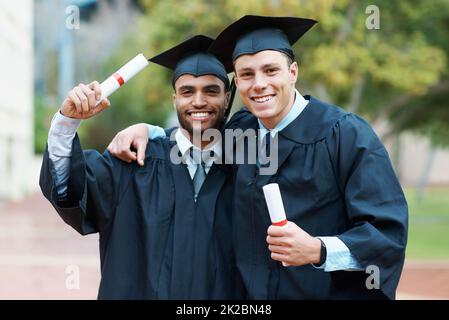 Nous étions sur la voie du succès. Deux jeunes diplômés de l'université détiennent leurs diplômes tout en portant une casquette et une robe. Banque D'Images