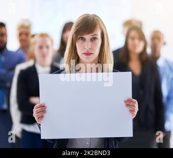 Nous avons un message. Portrait d'une femme d'affaires tenant un tableau blanc avec des collègues debout derrière elle. Banque D'Images
