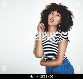 C'est un bon petit bonheur. Photo en studio d'une jeune femme qui colle sa langue sur un fond gris. Banque D'Images