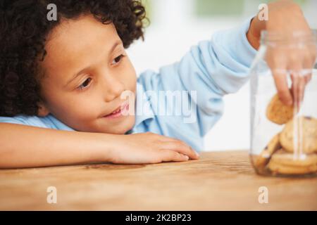 MMM, tellement de cookies juste pour moi. Un jeune garçon mignon saisissant un cookie du pot à biscuits. Banque D'Images