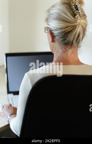 Connecté au monde depuis le confort de sa maison. Vue arrière d'une femme travaillant sur son ordinateur portable. Banque D'Images