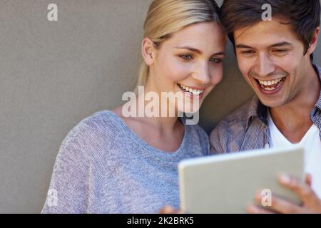 Nous avons beaucoup aimé pour cette photo. Photo d'un jeune couple heureux avec une tablette numérique sur fond gris. Banque D'Images