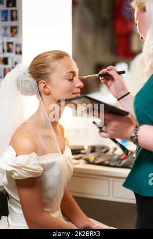 S'assurer qu'elle a l'air parfaite. Un artiste de maquillage appliquant le maquillage à une mariée. Banque D'Images