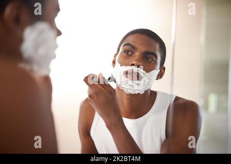 Se débarrasser des poils tenaces. Un jeune homme se raser dans le miroir. Banque D'Images