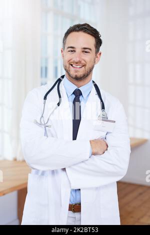 Nous allons mieux vous mettre en place. Portrait d'un jeune médecin confiant debout dans sa salle de consultation. Banque D'Images