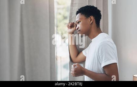 Un autre jour dans la vie du verrouillage. Photo d'un jeune homme ayant un café et regardant à l'extérieur de la fenêtre de sa chambre à coucher à la maison. Banque D'Images