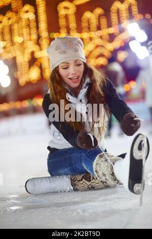 Presque là. Photo d'une jeune femme assise sur la glace d'une patinoire qui noue les lacets de ses patins à glace. Banque D'Images