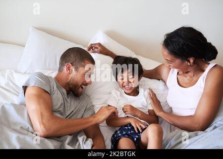 Il apporte la joie et le bonheur dans nos vies. Photo d'une belle jeune famille de trois personnes qui passent du temps ensemble dans leur chambre à la maison. Banque D'Images