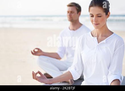 Yoga en bord de mer. Un jeune couple pratiquant le yoga sur la plage. Banque D'Images