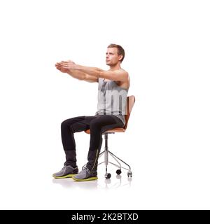 Garder ses membres longs et maigres. Un beau jeune homme portant des vêtements de gym et s'étirant tout en étant assis dans une chaise de bureau sur un fond blanc. Banque D'Images