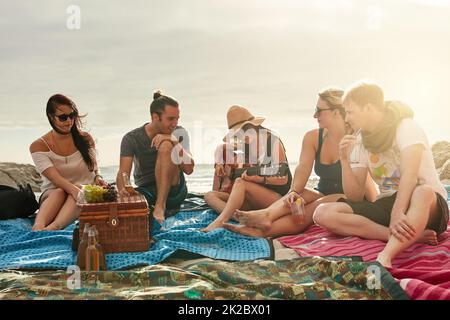 Nos meilleurs souvenirs sont faits sur la plage. Photo d'un groupe de jeunes amis heureux profitant d'un pique-nique sur la plage ensemble. Banque D'Images