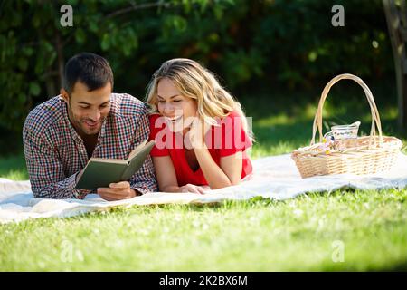 Couples qui rient ensemble Photo d'un jeune couple heureux lisant un livre tout en ayant un pique-nique dans un parc. Banque D'Images