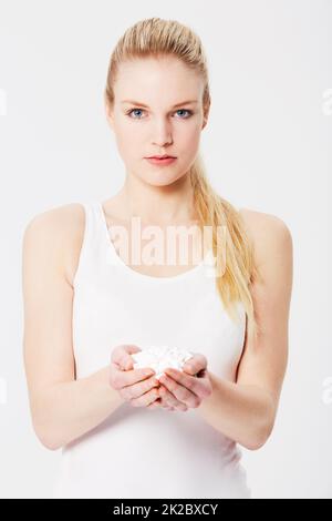 Trop de médicaments peuvent vous rendre malade. Portrait d'une fille caucasienne sérieuse tenant une main pleine de pilules contre un fond isolé. Banque D'Images