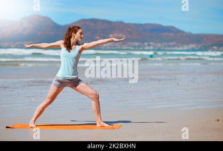 Soyez un guerrier pas un plus adoreur. Photo d'une jeune femme pratiquant sa routine de yoga à la plage. Banque D'Images