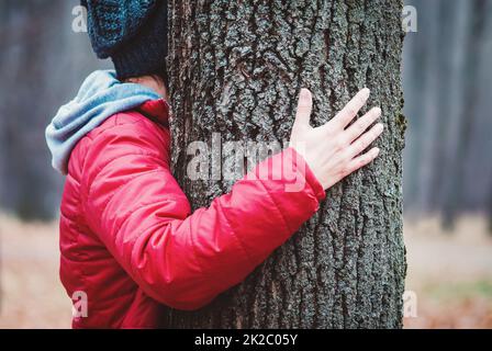 Hugging tree trunk in autumn park, woman embraces old tree outdoors, love and unity with nature Banque D'Images