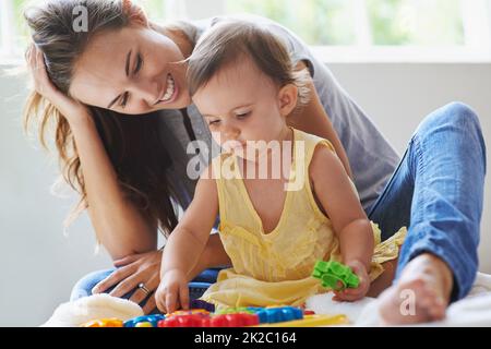 Shes un peu de génie déjà. Photo d'une petite fille mignonne assise sur le sol avec sa mère et jouant avec des jouets. Banque D'Images