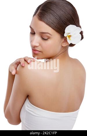 Shes a une peau magnifique. Studio photo d'une belle jeune femme avec une orchidée dans ses cheveux regardant au-dessus de son épaule. Banque D'Images