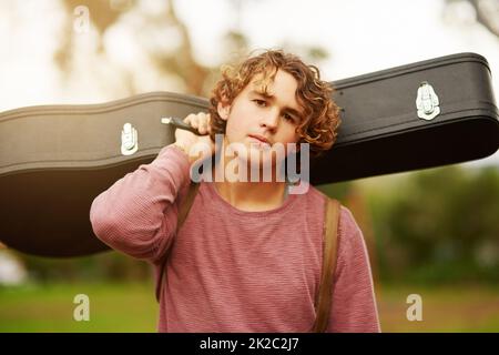 Je vais partout avec ma guitare. Portrait d'un jeune homme debout à l'extérieur portant une sacoche de guitare sur son épaule. Banque D'Images