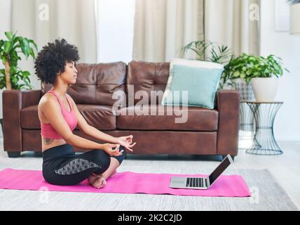 Je prends des cours de mon influenceur préféré. Photo d'une belle jeune femme utilisant son ordinateur portable tout en pratiquant le yoga à la maison. Banque D'Images