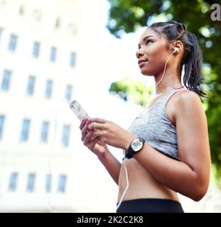 Cette chanson me met toujours dans une humeur active. Prise de vue d'une jeune femme attrayante écoutant de la musique et utilisant son téléphone portable tout en s'exerçant à l'extérieur dans la ville. Banque D'Images