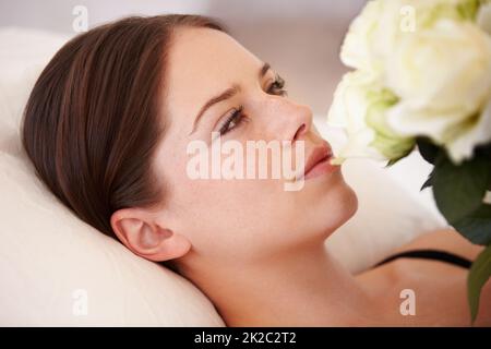 Son cœur est gagné. Une belle jeune femme couchée et admirant le bouquet de roses blanches qu'elle tient. Banque D'Images