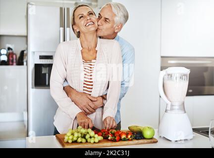 Merci de nous avoir pris soin de nous. Plan court d'un beau homme mûr embrassant sa femme pendant qu'elle prépare un repas sain à la maison. Banque D'Images