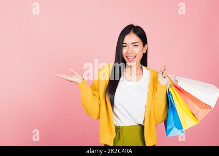 femme shopper souriant debout tenant des sacs de shopping multicolore en été montrer quelque chose main palmier Banque D'Images