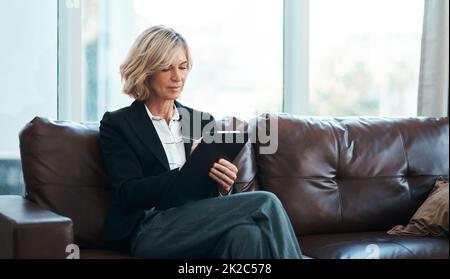 Le meilleur dans le domaine de la santé mentale. Photo d'un psychologue mature assis sur un canapé et écrivant des notes sur un presse-papiers. Banque D'Images