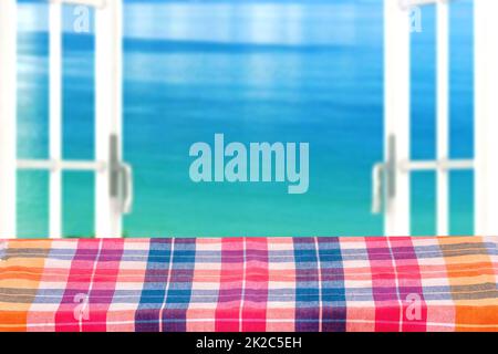 Produit de table vide. Table en bois vide recouverte d'une nappe colorée à carreaux sur un arrière-plan abstrait flou de l'océan. Espace pour le montage de vos produits alimentaires. Banque D'Images