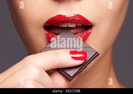 Chaque femme a besoin d'un jour de chocolat sans culpabilité. Portrait en gros plan d'une jeune femme mignonne mordant sur une barre de chocolat. Banque D'Images