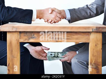 Transactions sous-table Plan court de deux hommes d'affaires qui se secouent la main tandis que l'argent passe la main sous une table. Banque D'Images